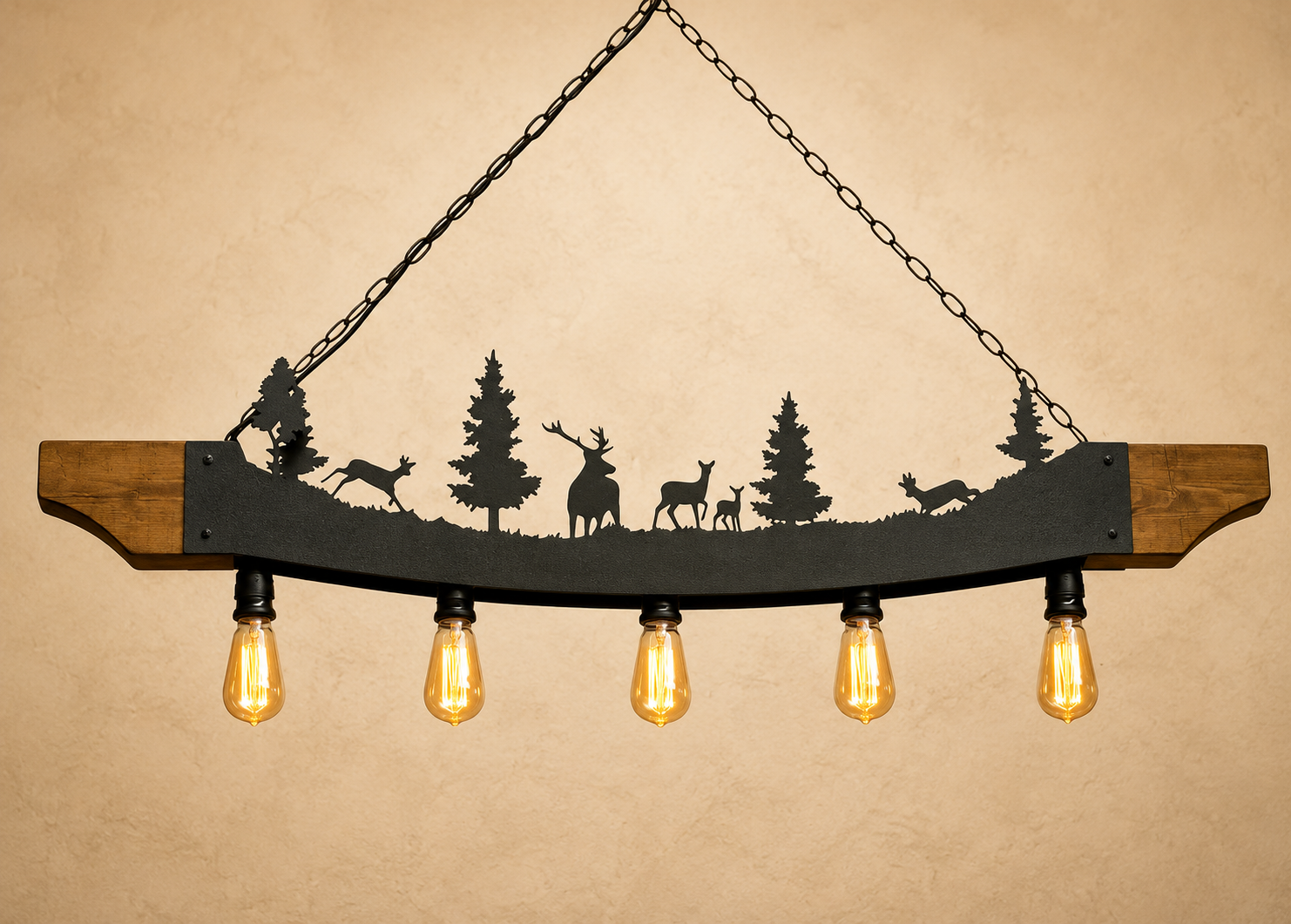 A rustic hanging light fixture with a curved wooden bar, black metal silhouette of deer and trees, and five glowing warm Edison bulbs against a beige textured background.