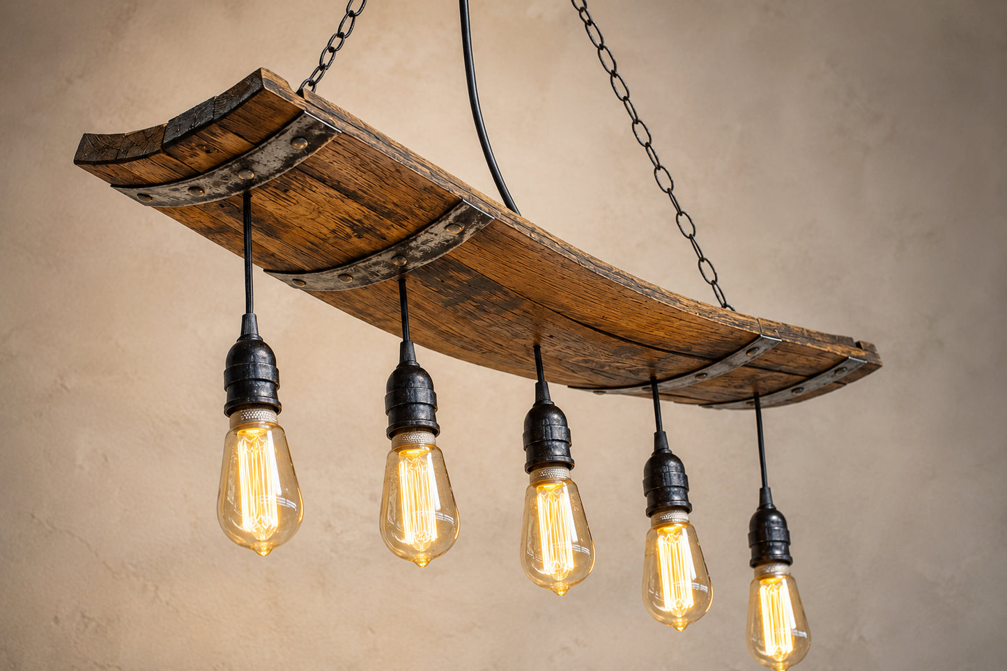 A rustic wine barrel-style chandelier featuring a curved wooden barrel taves with metal rebar reinforcement and five hanging Edison-style light bulbs.