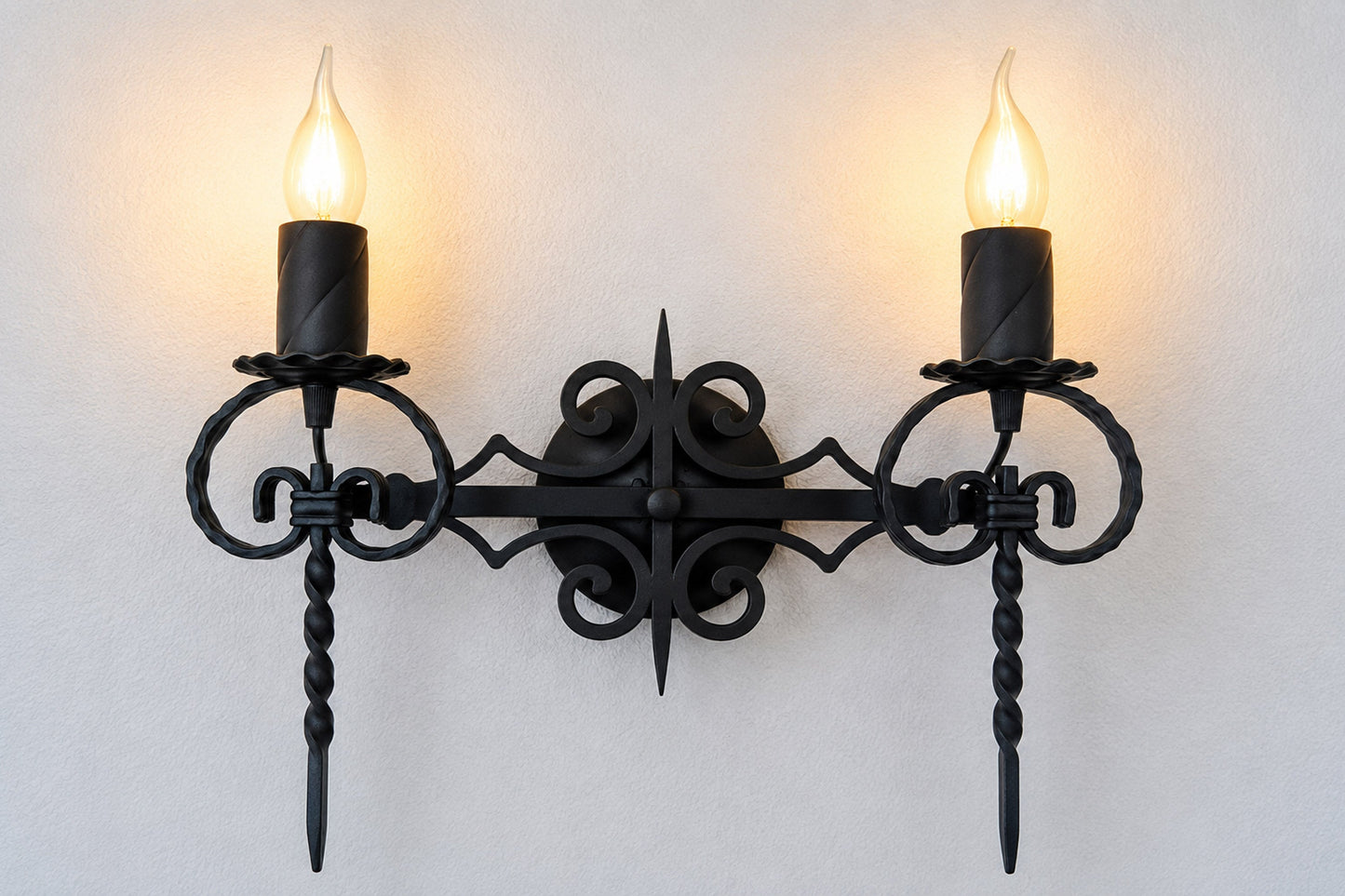 Decorative black wall sconce with two lit candles on a light background