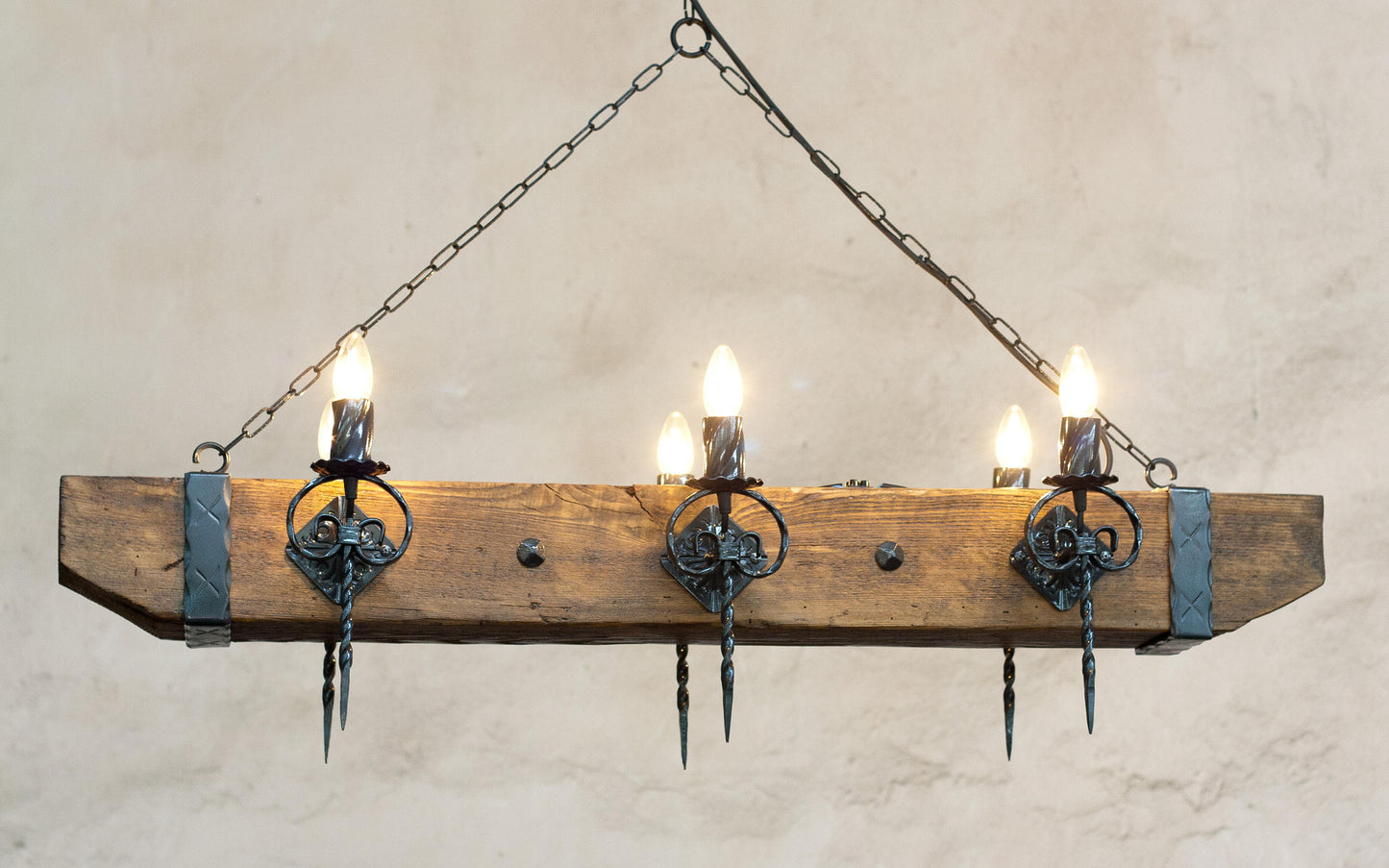 A rustic wood beam and wrought iron chandelier with multiple light bulbs, hanging against an indoor background.
