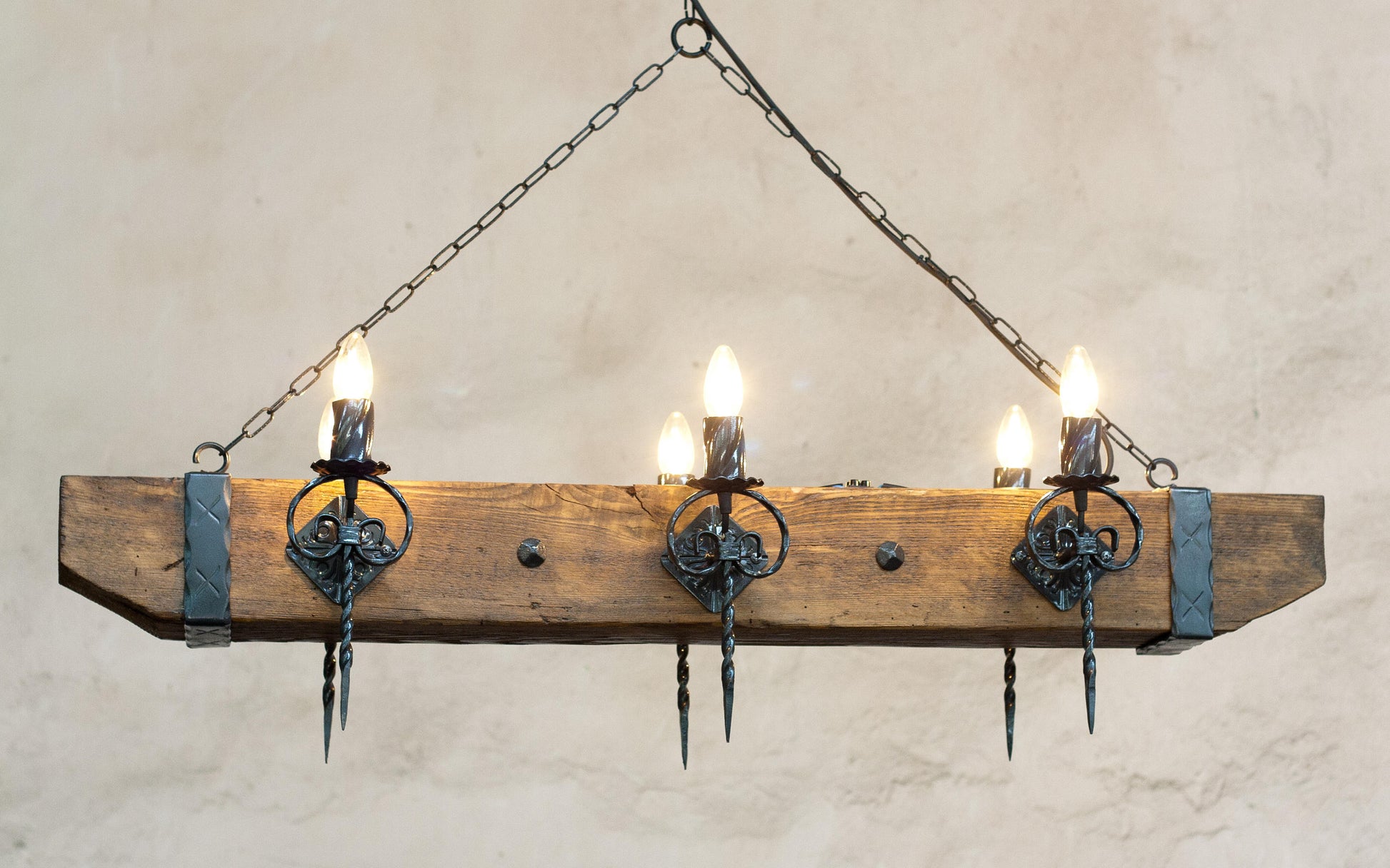 A rustic wood beam and wrought iron chandelier with multiple light bulbs, hanging against an indoor background.