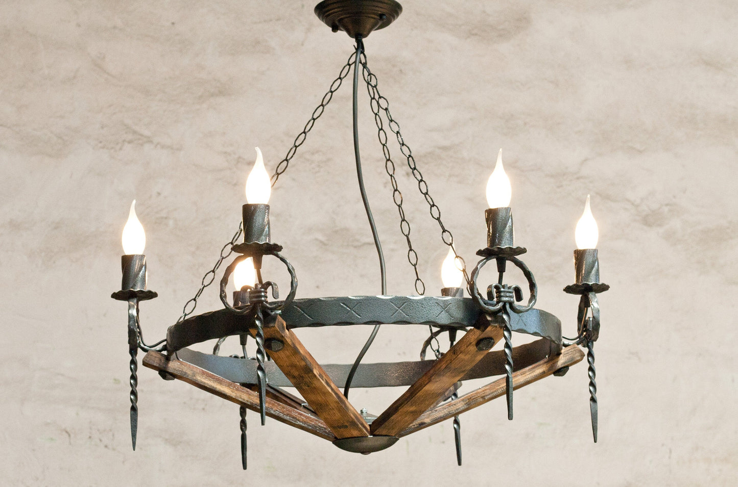 A rustic chandelier featuring wrought iron with a hammered black finish, and elements that resemble wood staves.