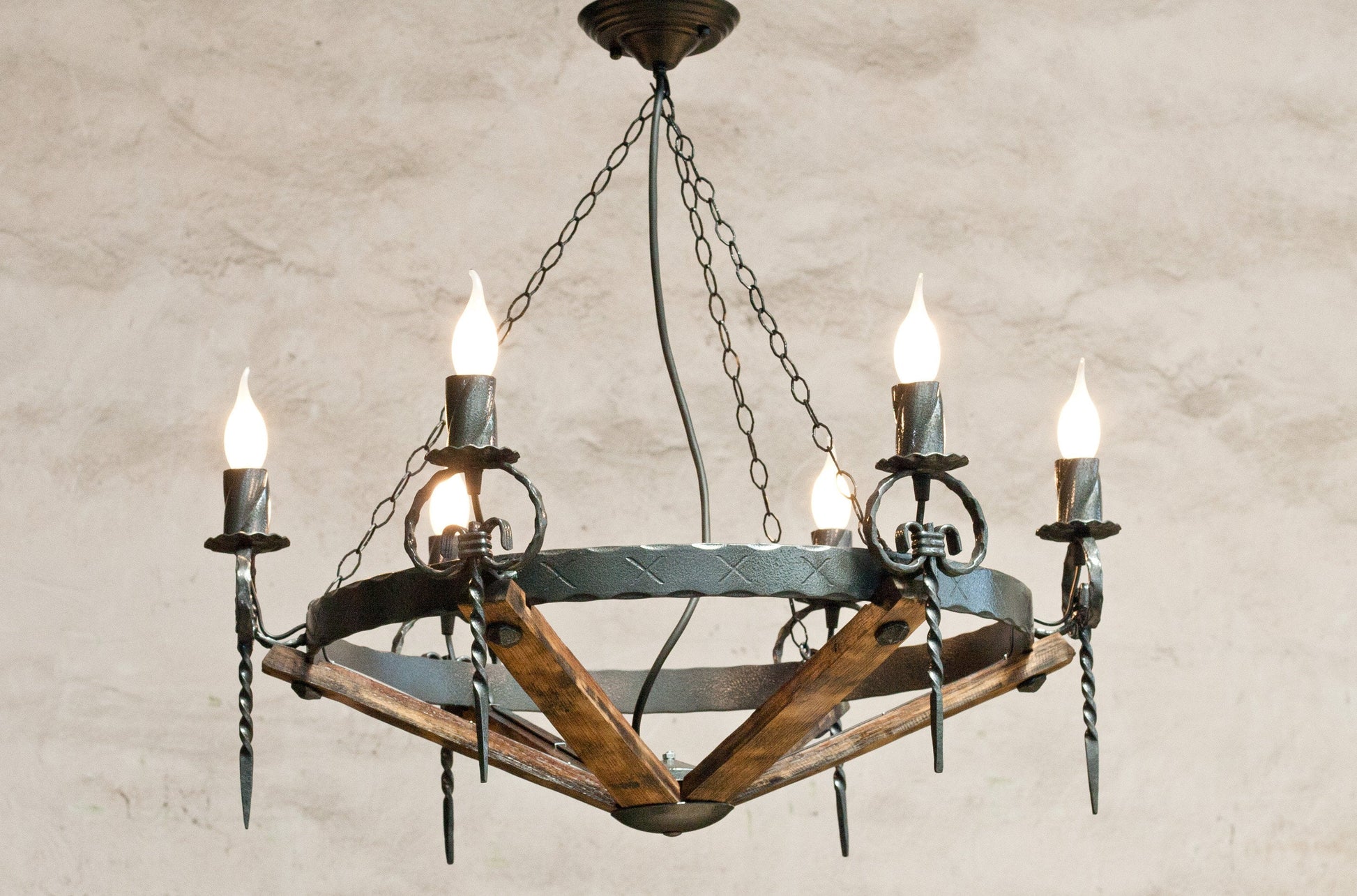 A rustic chandelier featuring wrought iron with a hammered black finish, and elements that resemble wood staves.