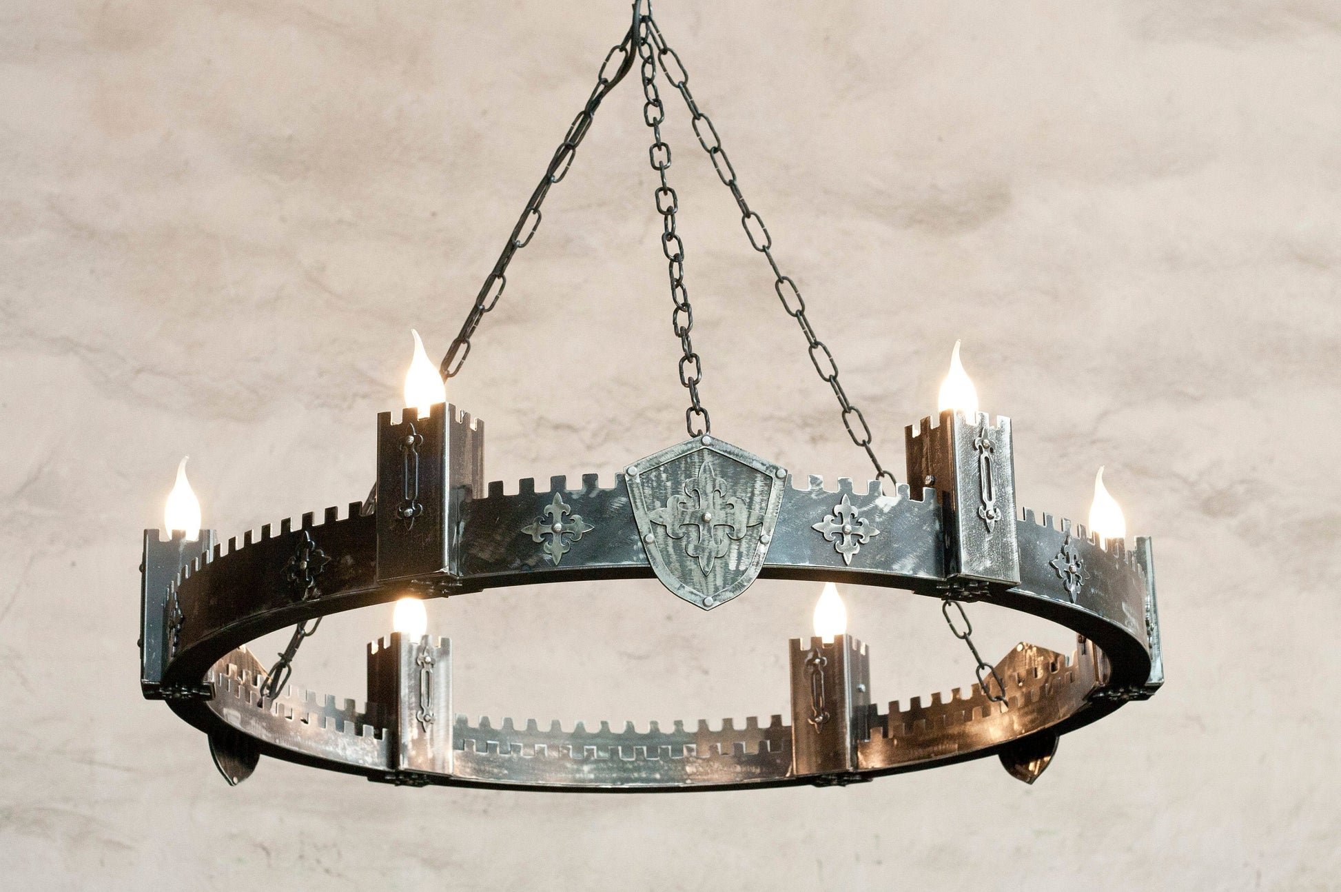 An iron chandelier with a medieval castle style, featuring a circular structure with six protruding towers, made of two layers of steel with a bare metal finish.
