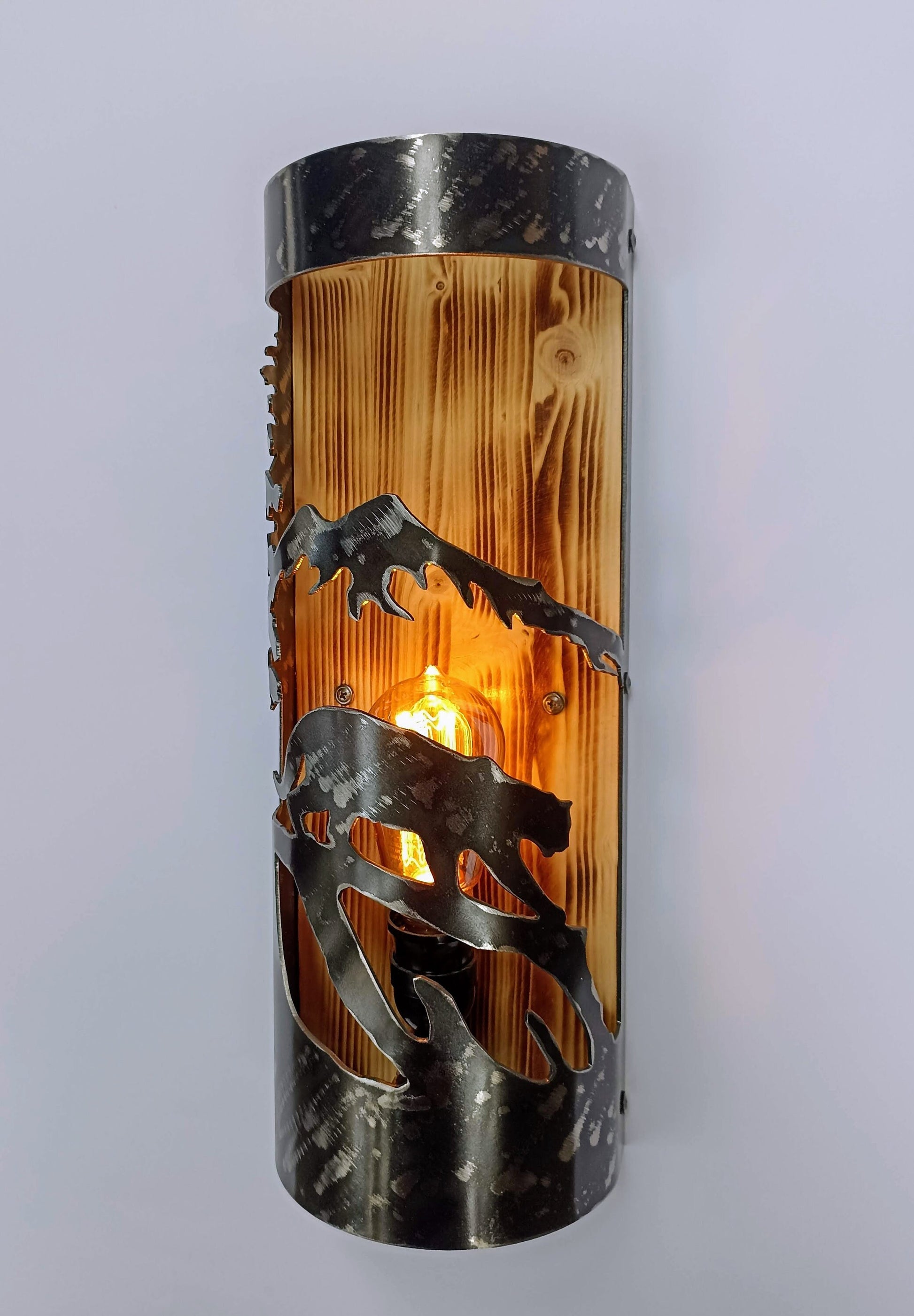 A rustic style wall light featuring a mountain lion design, made out of wood and steel with a burned wood finish on the wood and a clear coat finish on the steel.