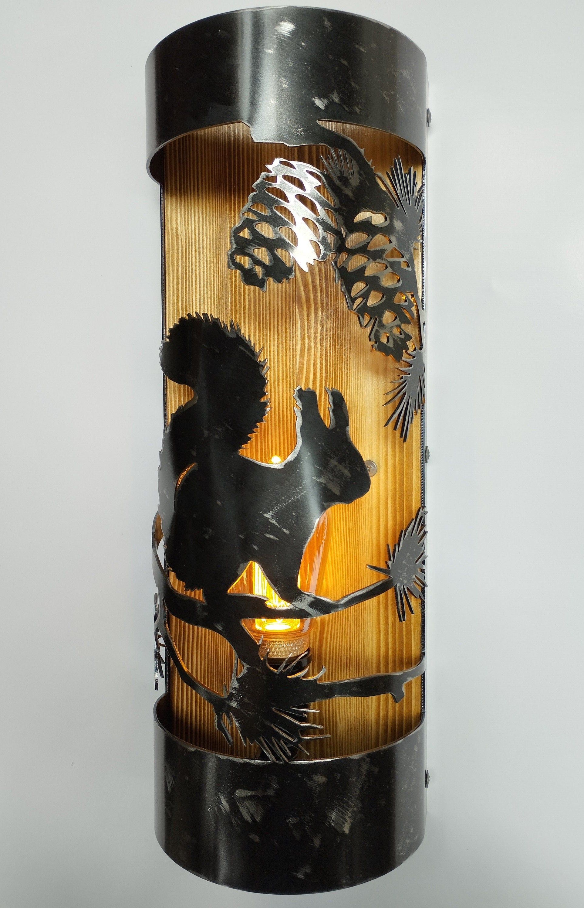 A rustic wall light fixture with a silhouette of a squirrel and pine cones, made of wood and metal with a clear coat finish.